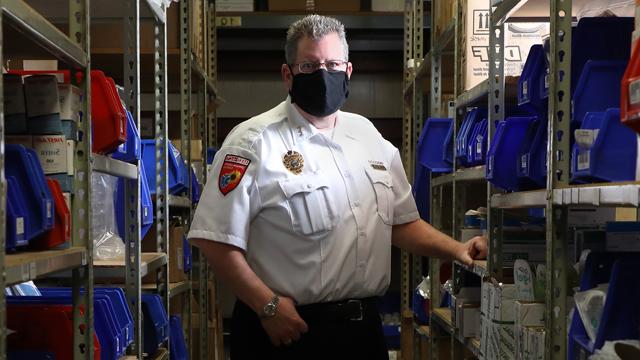 Brad Mason, wearing a mask, and standing in a storeroom of medical supplies