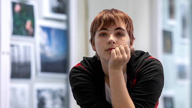 Liberty Wheatley looks at the camera, learning forward on her hand, with blurred artwork displayed on walls in the background.